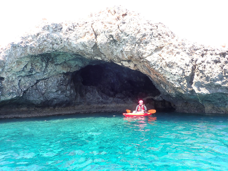 A kayaker next to a tiny cave in light blue waters