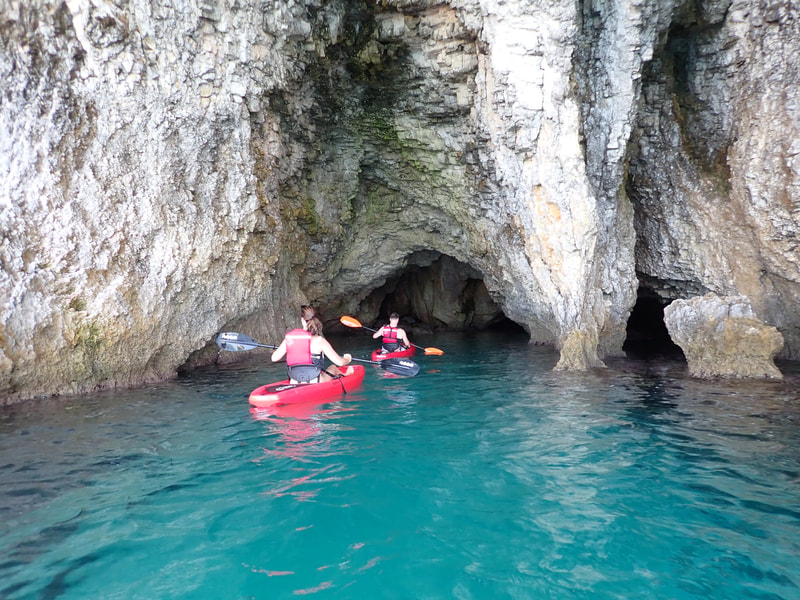 Two kayakers entering a sea cave with light blue waters
