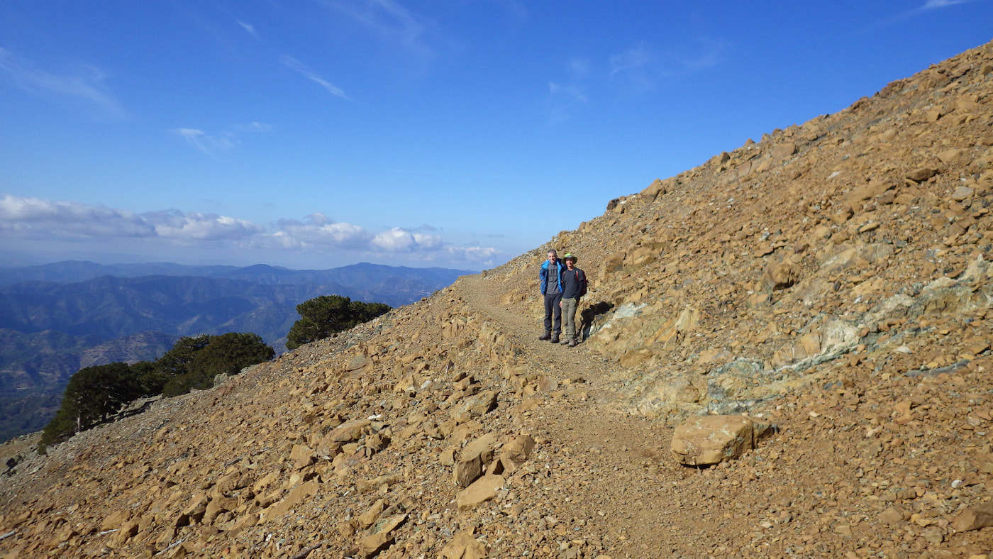 Two walkers standing on a flat trail on a steep slope