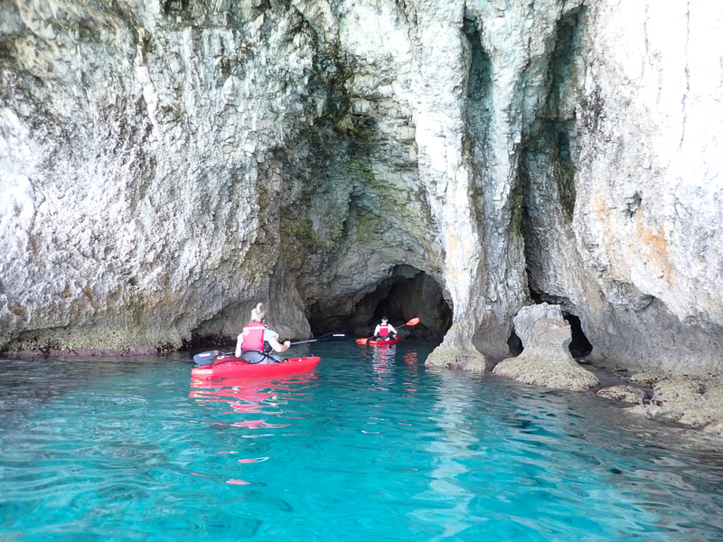 2 kayakers entering a sea cave with light blue waters on single red sitontop kayaks