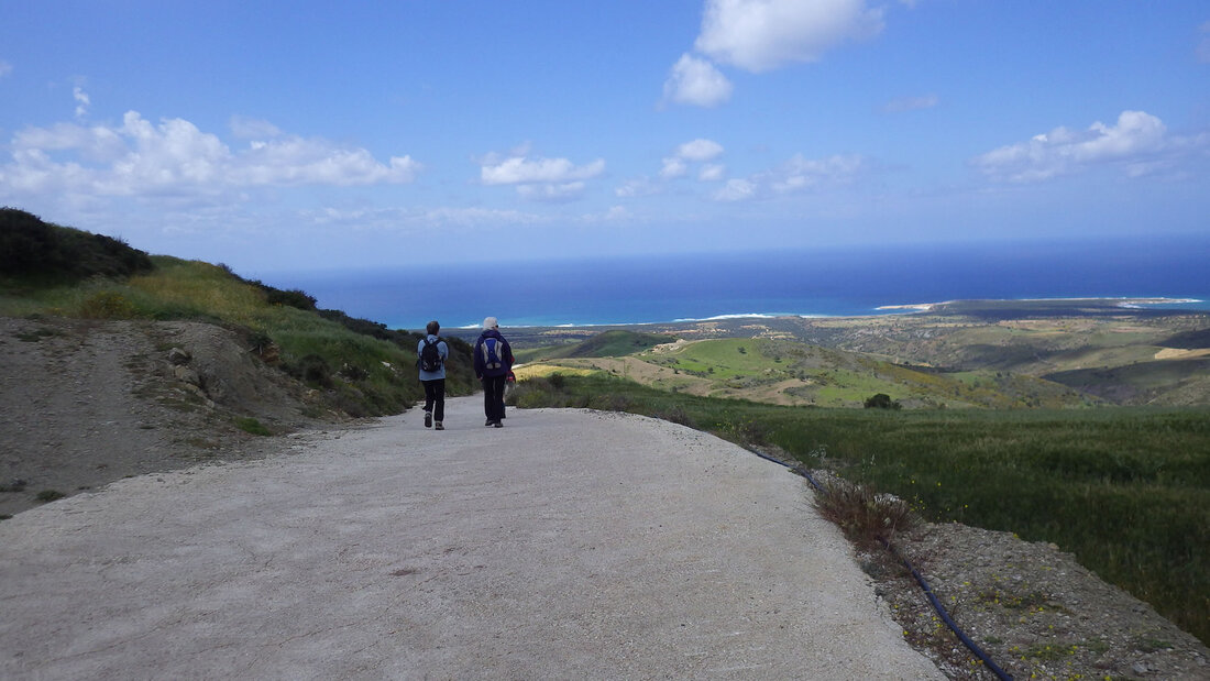 Two walkers on a cement road descending to the coast
