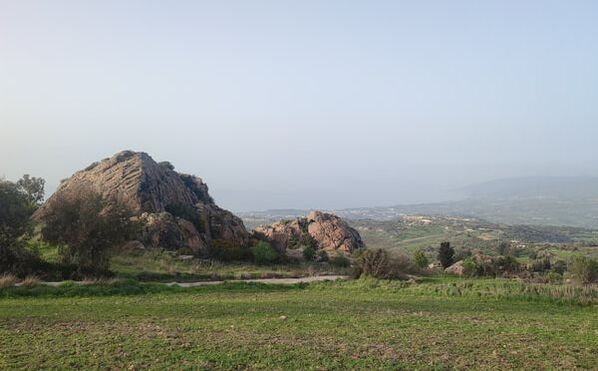 Boulders in green fields in the foreground. A bay far away in the background